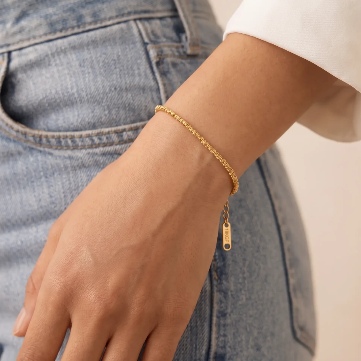 Model draagt de Shimmer Chain Bracelet: getextureerde gouden schakelarmband om de pols