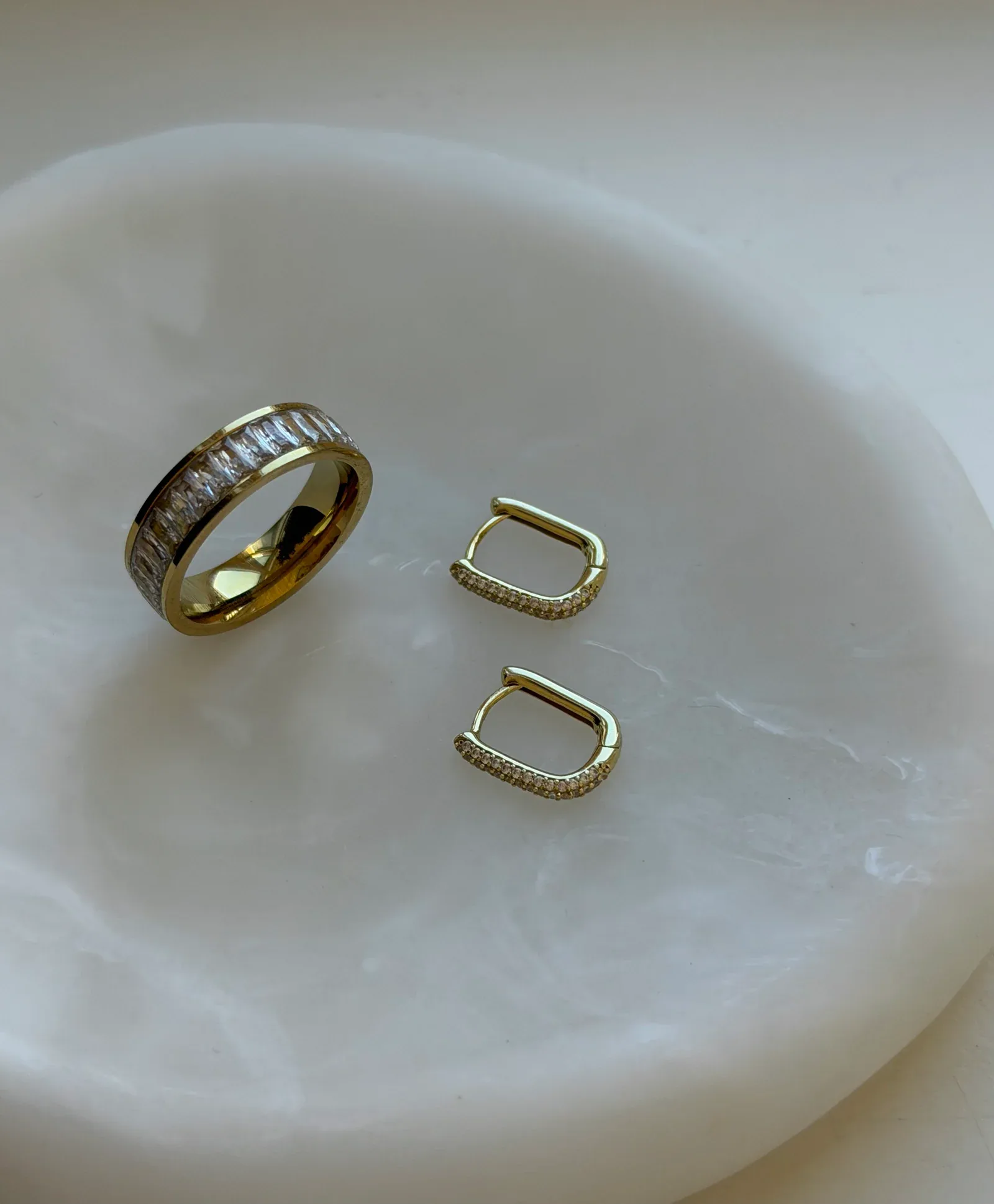 De Capsule Pavé Huggies naast de Eternity Ring op een wit sieradenschaaltje