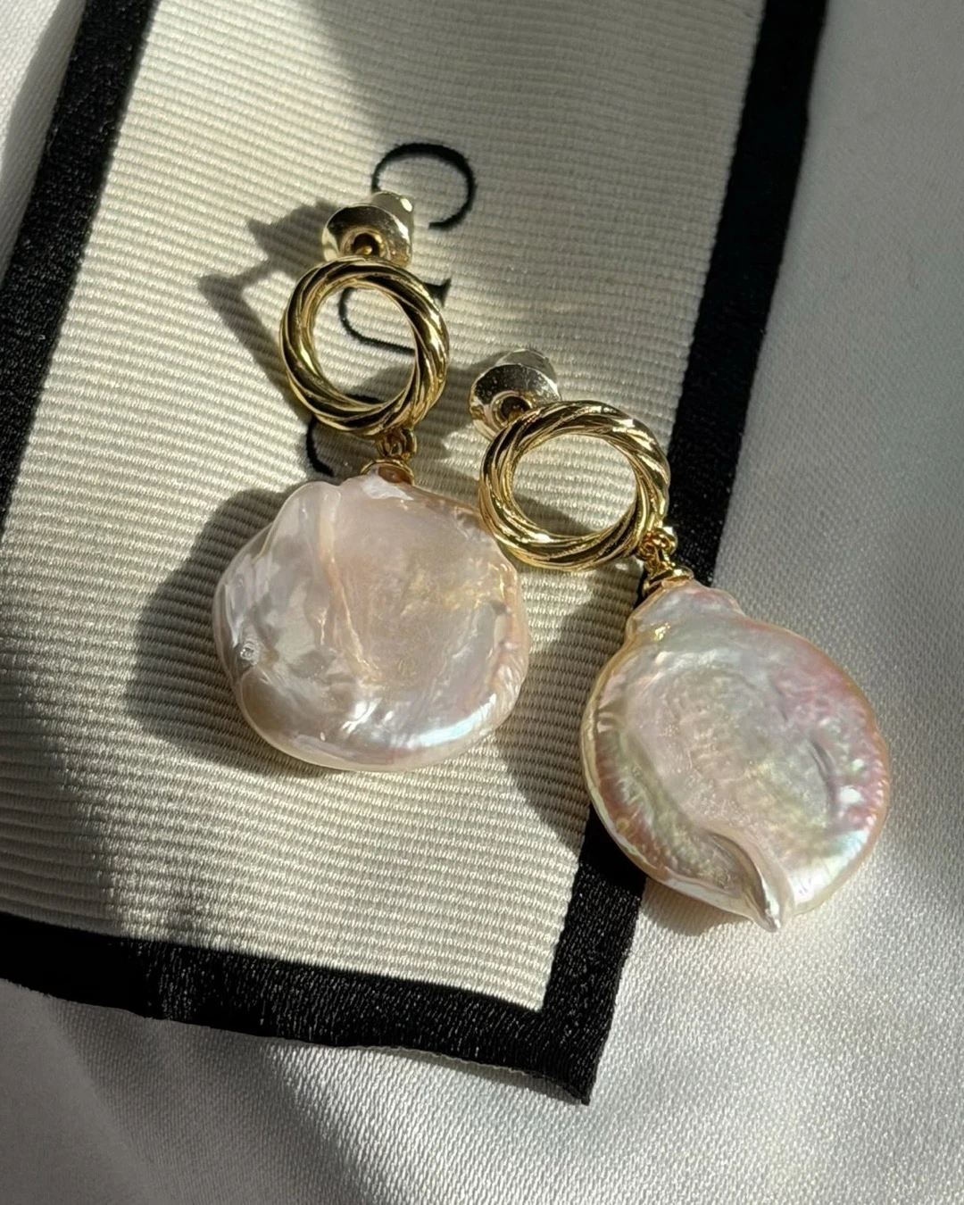 De Baroque Pearl Drops op een crème sjaal met zwarte rand: gedraaide gouden ringetjes met barokparel