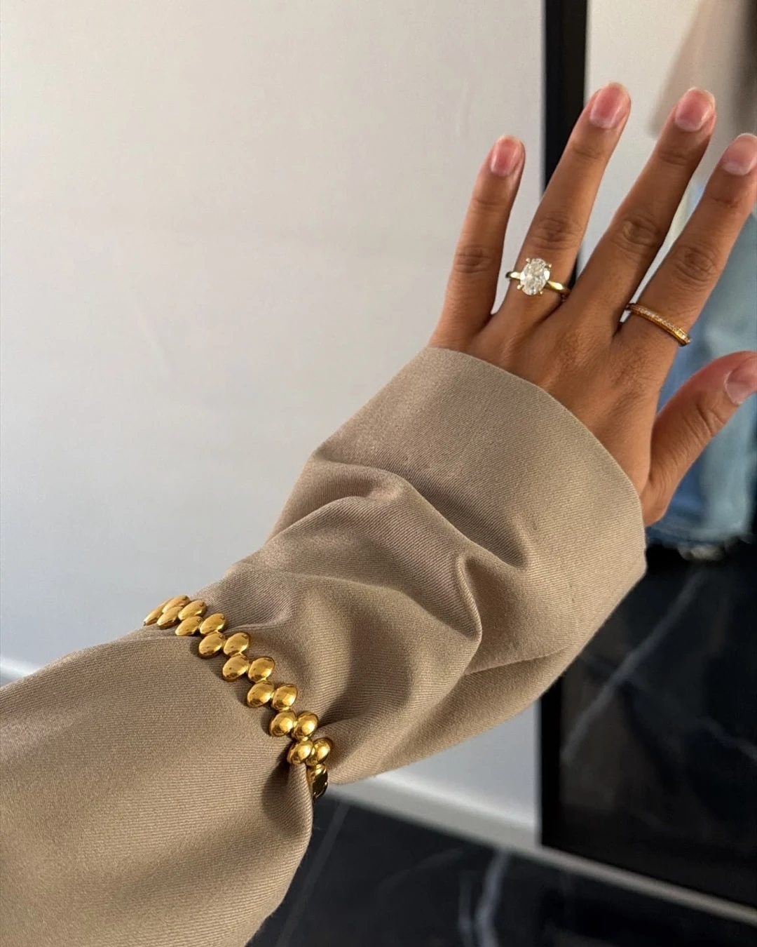 Hand tegen een spiegel met de Fluted Pavé Ring om de wijsvinger en de gouden Pebble Row Bangle over een beige mouw