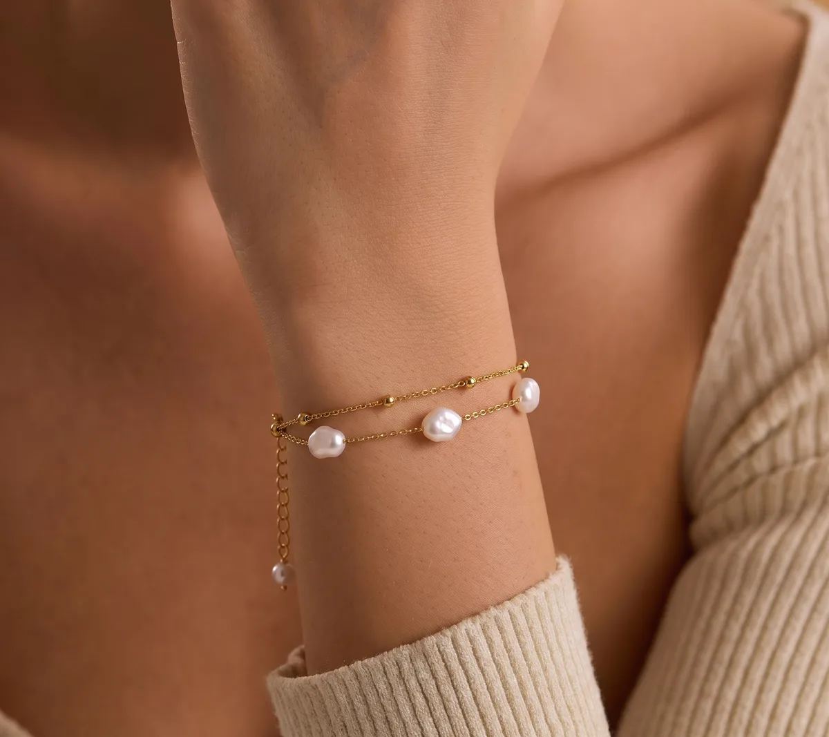 De Pearl Duo Bracelet om de pols, bij een crèmekleurige gebreide trui