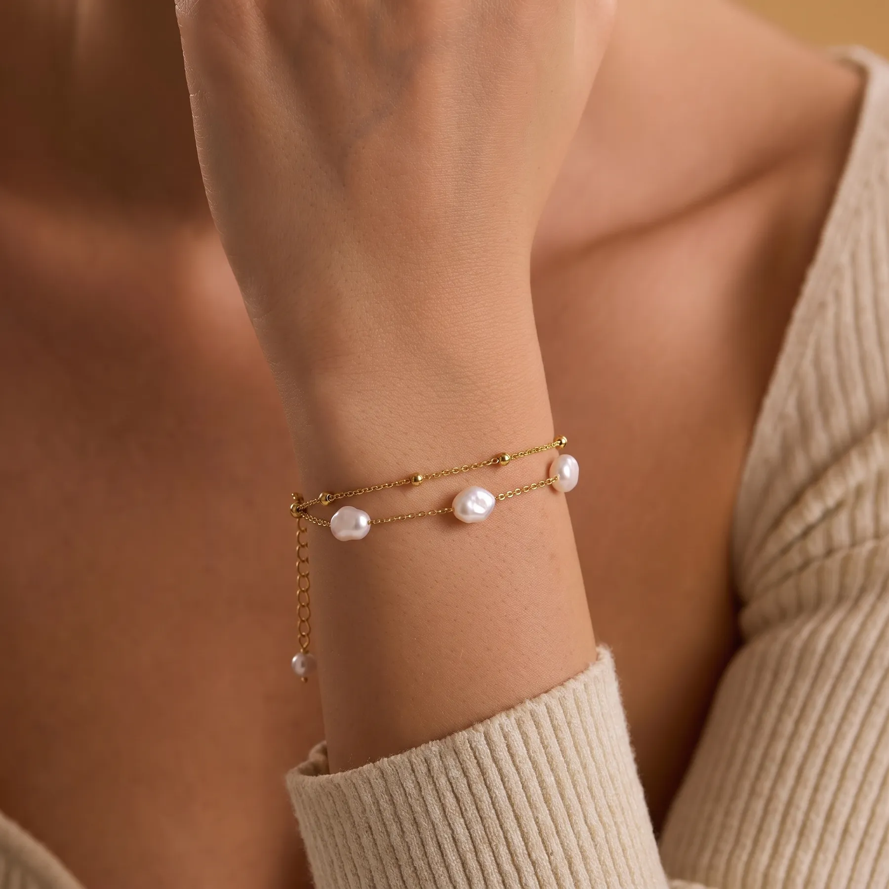 De Pearl Duo Bracelet om de pols, bij een crèmekleurige gebreide trui
